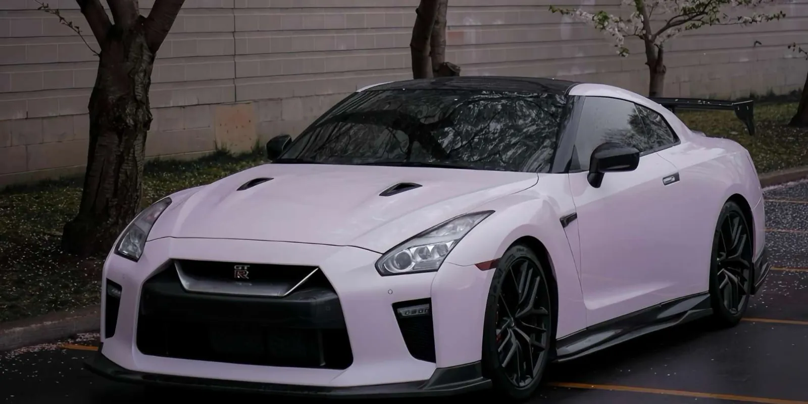 Pale pink Nissan GT-R R35 parked streetside under spring blossoms