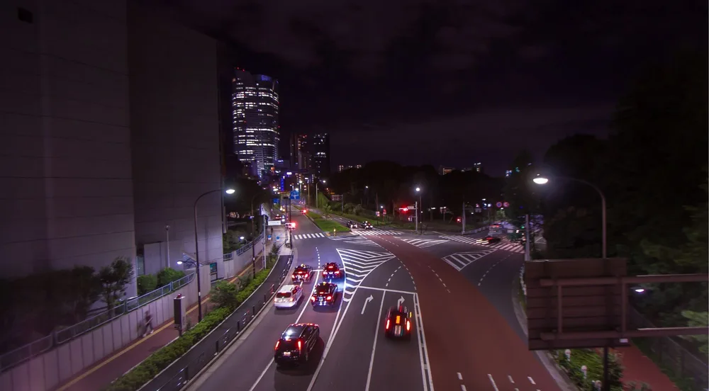 Nighttime Tokyo intersection near Roppongi with car light trails and a lit-up skyscraper backdrop