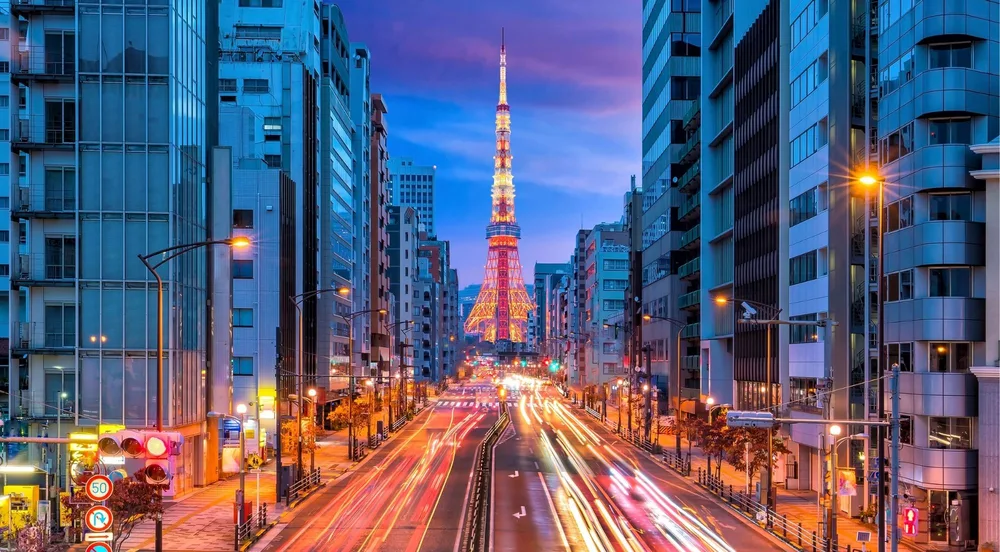 Tokyo Tower lit up at night at the end of a busy avenue, one of the photo-stop landmarks on the route