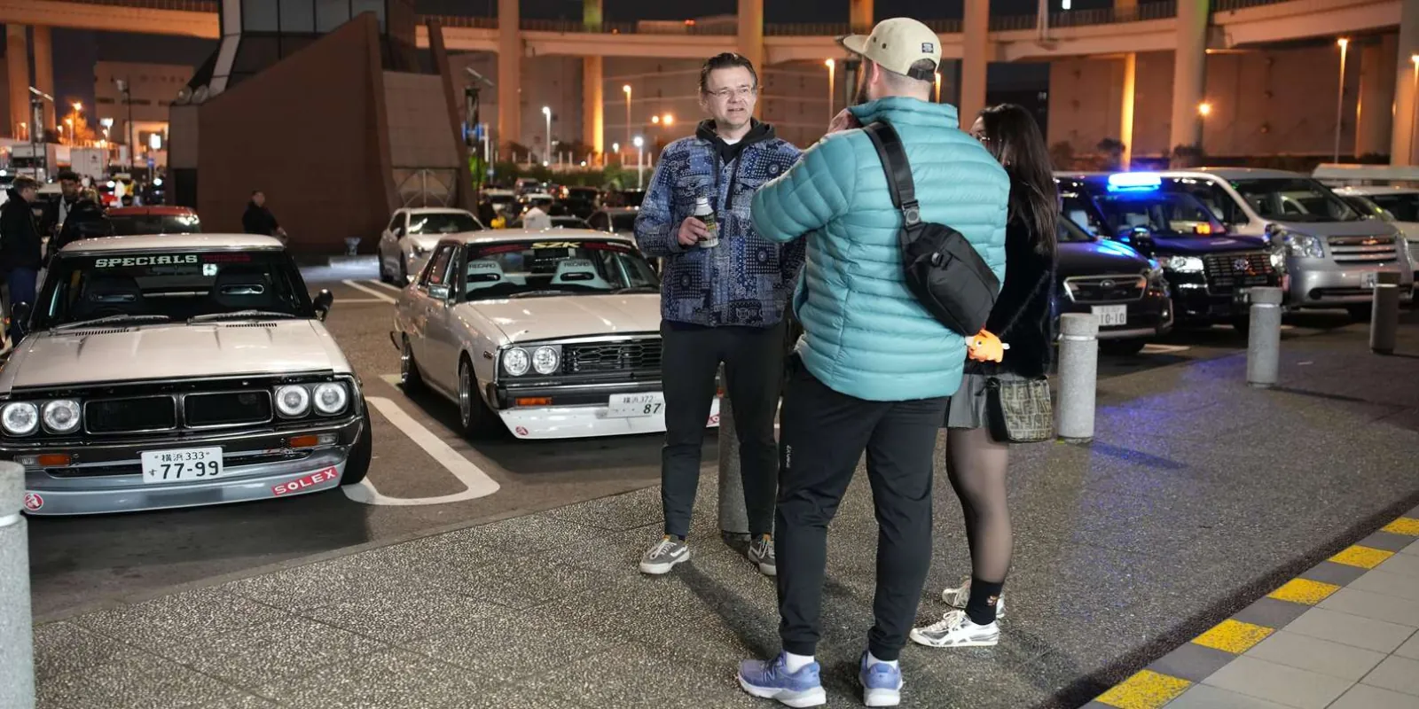 Guests and a guide talking JDM builds beside a row of classic tuned Skylines