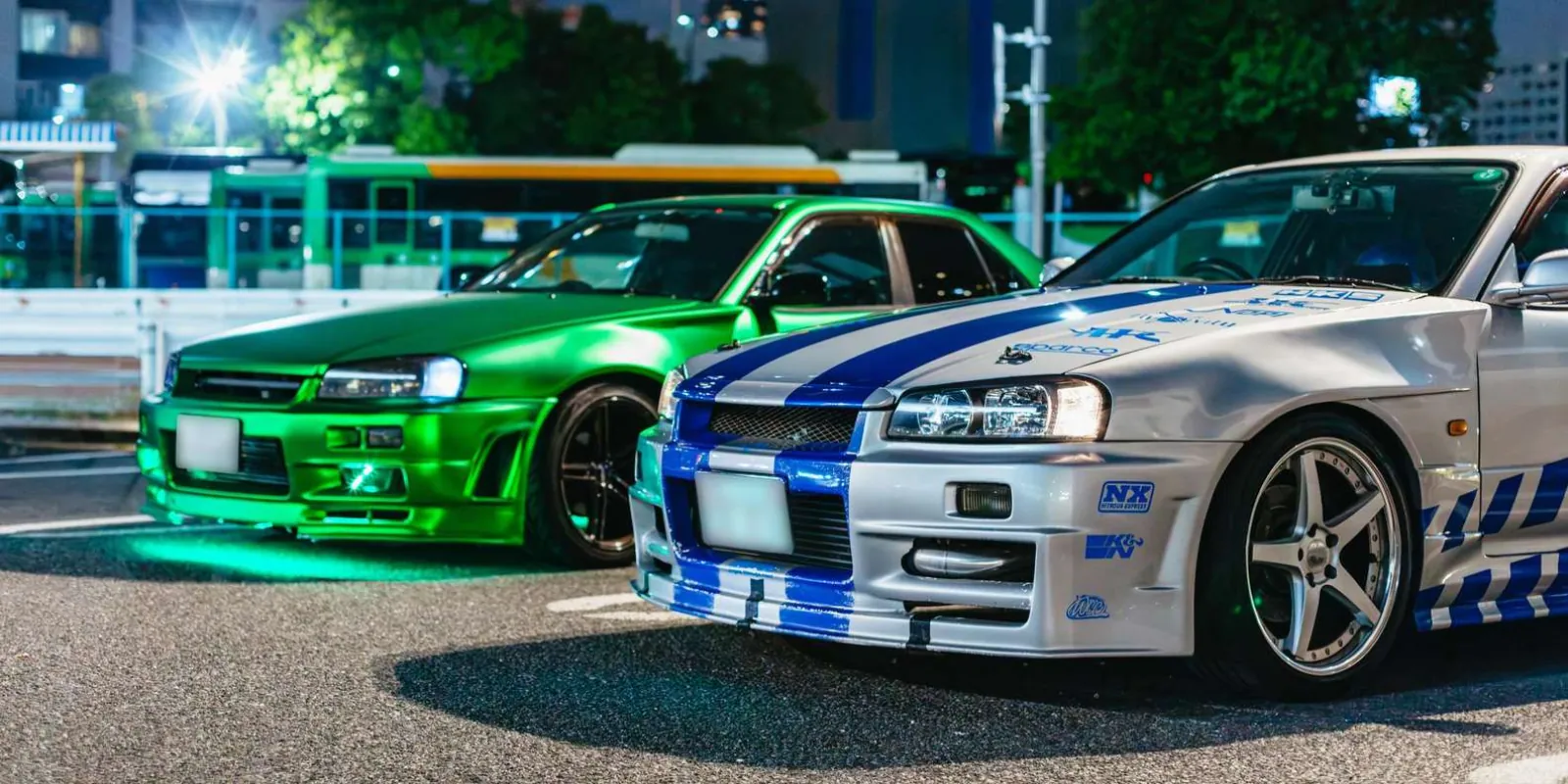 Modified silver and white Nissan Skyline GT-R R34s parked side by side under Daikoku Parking Area's lights