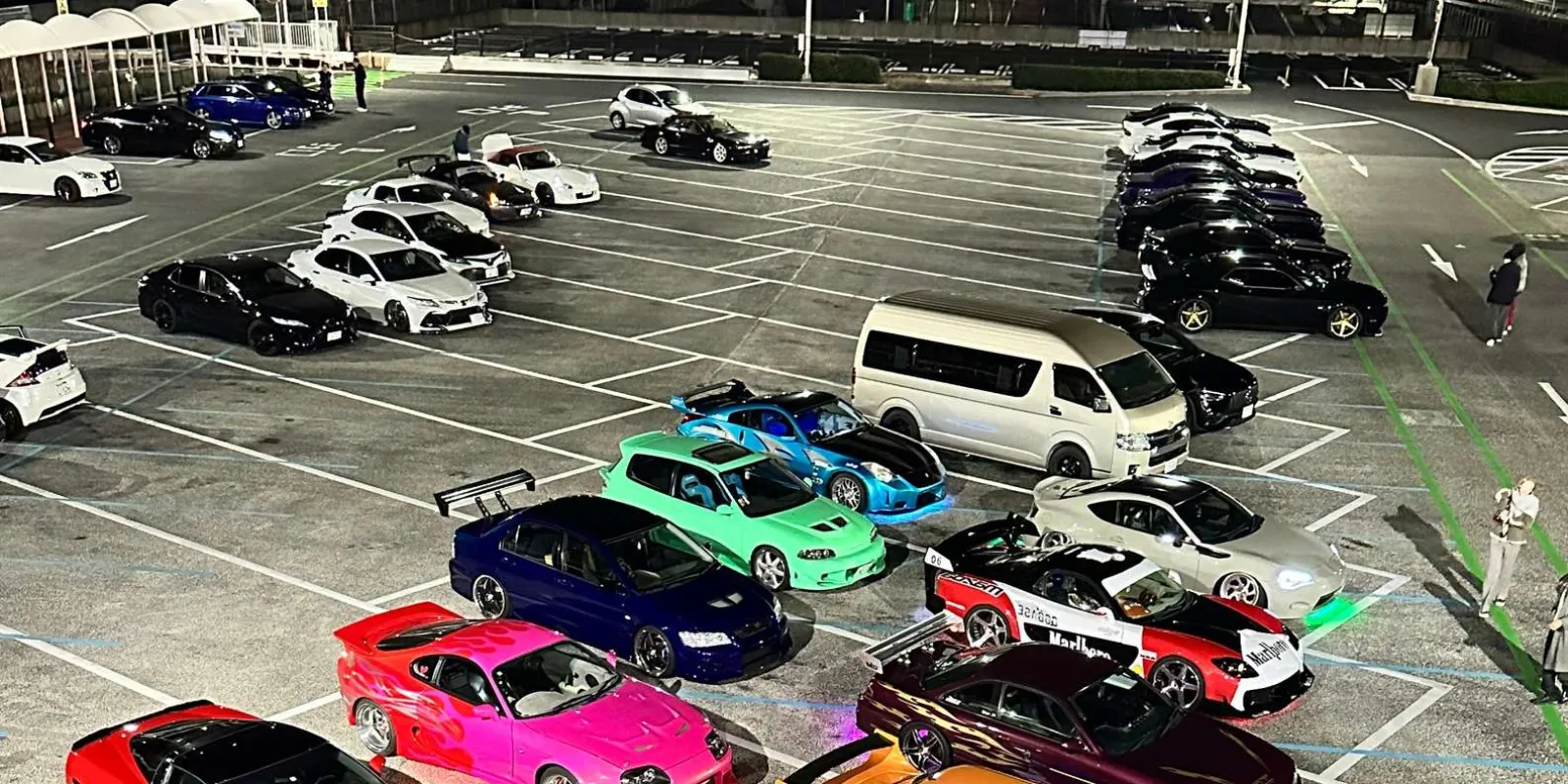 Colorful lineup of tuned JDM coupes and sedans packed into a Tokyo parking area at night