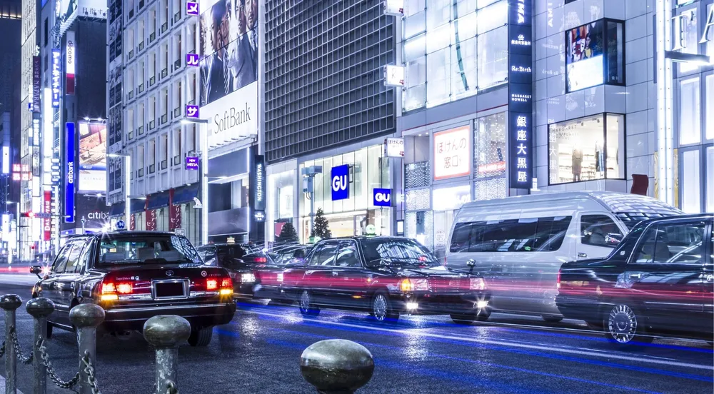 Line of black Toyota Crown sedans in Ginza traffic at night, downtown Tokyo backdrop