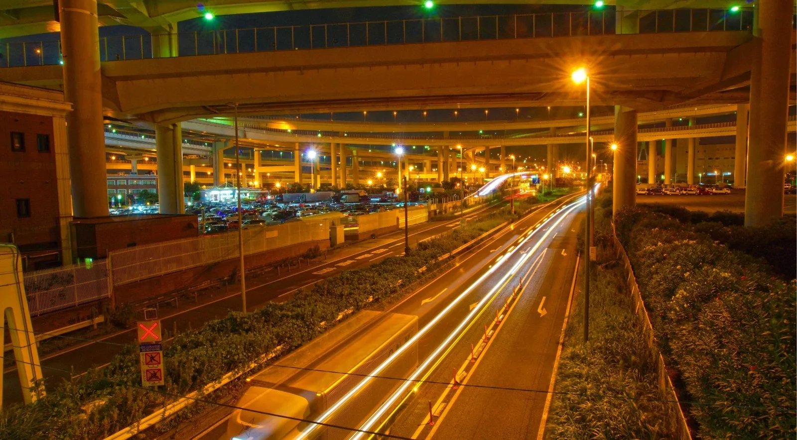Daikoku Parking Area's stacked highway ramps lit up at night, the legendary meet-up spot for Tokyo's JDM scene